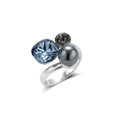 Adjustable ring with blue cushion-cut zirconia, gray pearl, and dark crystal on platinum-plated copper band against beige background.