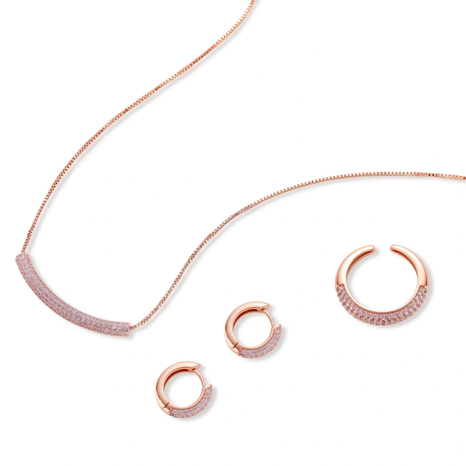 Rose gold pavé zirconia bar necklace, hoop earrings, and open ring set with pink stones on cream background.