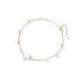 Delicate gold chain bracelet with baroque pearl centerpiece and small freshwater pearls on cream background.