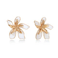 White enamel tropical flower earrings with sculptural gold-plated center and organic petal design on cream background
