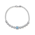 Sterling silver tennis bracelet with round halo-set moissanite stones and blue center stone on cream background.